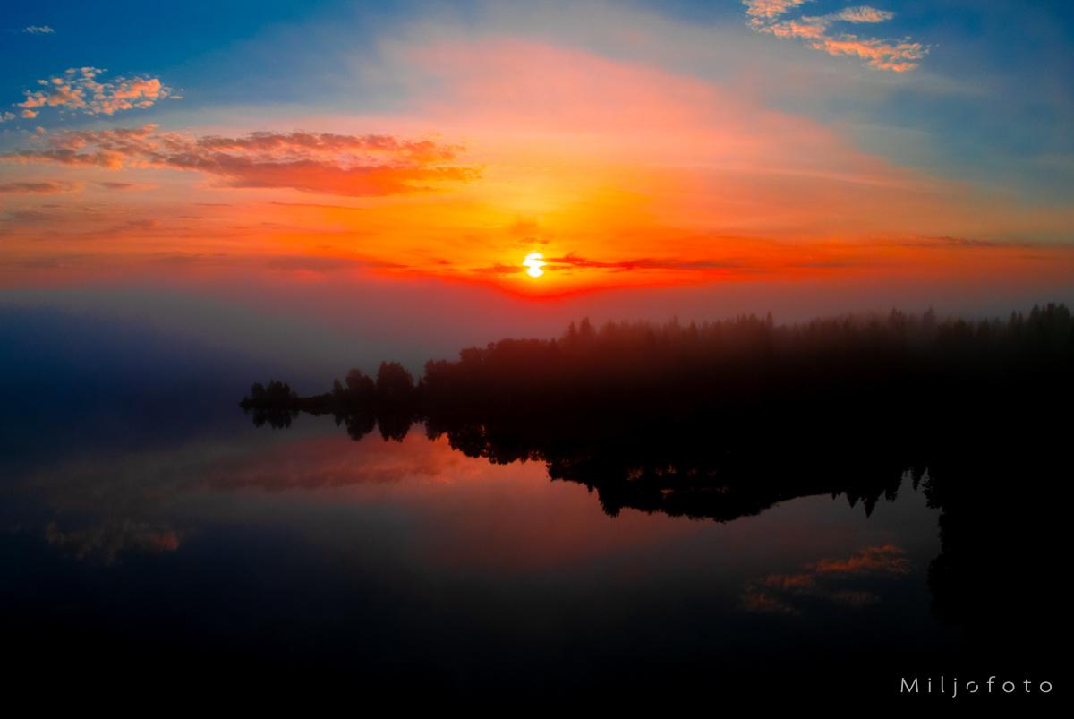 Solnedgang over sjø og skog