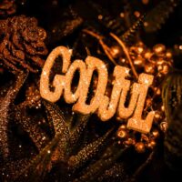 "Stemningsfullt bilde med teksten 'God Jul' i glitrende gull, omgitt av dekorative kongler og planter, med varme gyldne toner som skaper en koselig juleatmosfære."