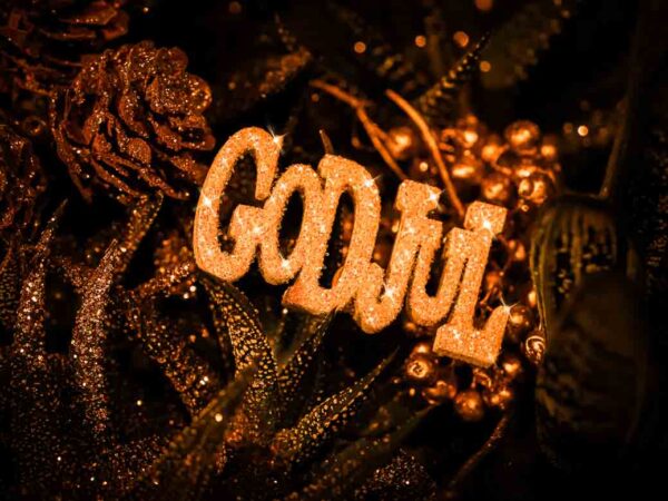 "Stemningsfullt bilde med teksten 'God Jul' i glitrende gull, omgitt av dekorative kongler og planter, med varme gyldne toner som skaper en koselig juleatmosfære."