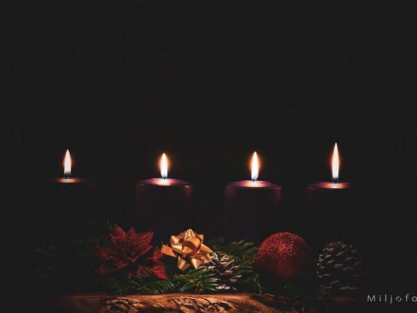 Bilde av fire lys som brenner i mørket, julepynt og grønne kvister