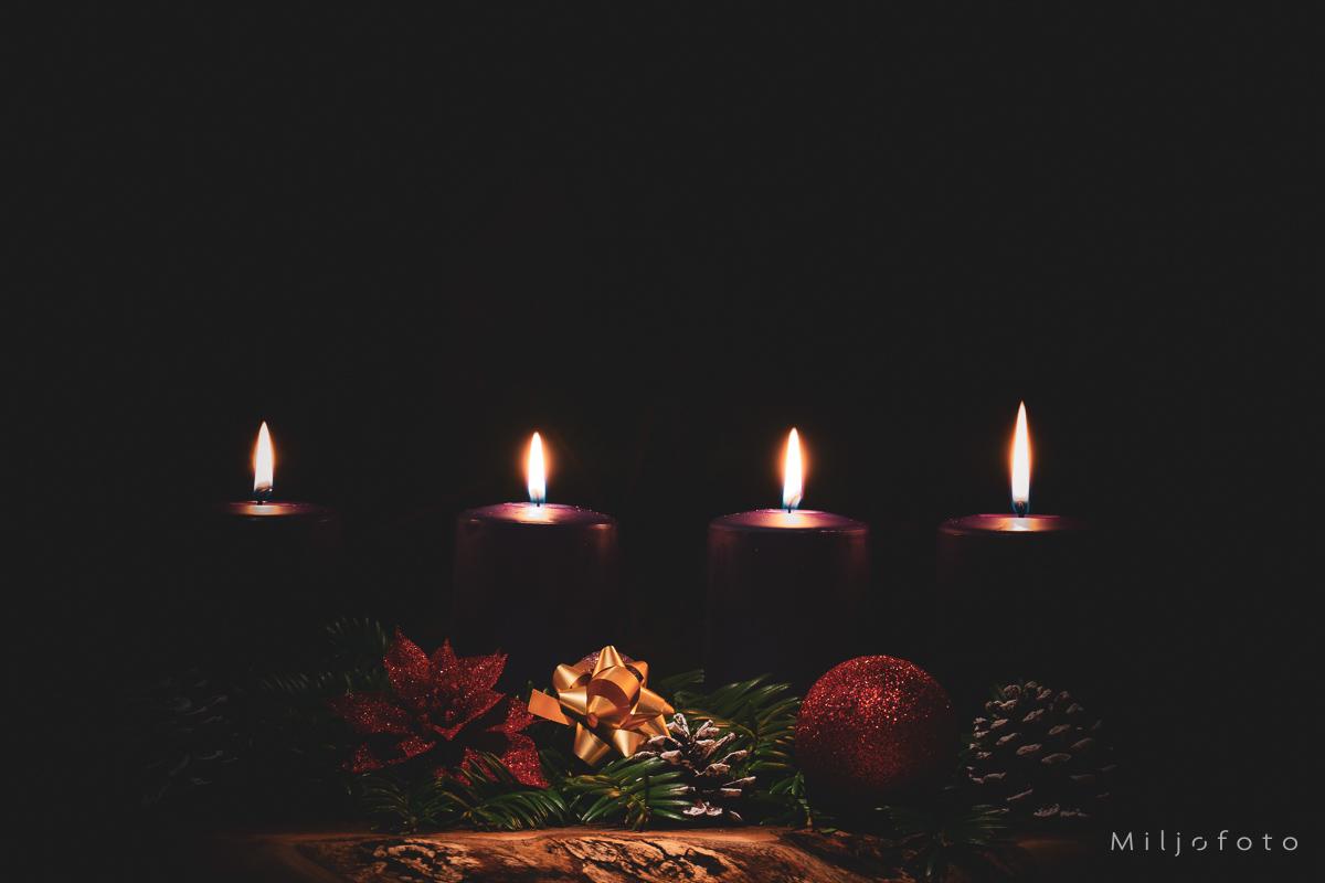 Adventsstake (4) Bilde av fire lys som brenner i mørket, julepynt og grønne kvister