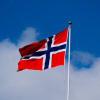 Norsk flagg i vinden med blå himmel.