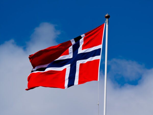 Norsk flagg i vinden med blå himmel.