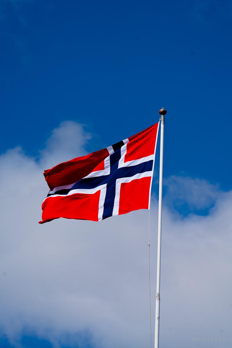Norsk flagg i vinden med blå himmel.