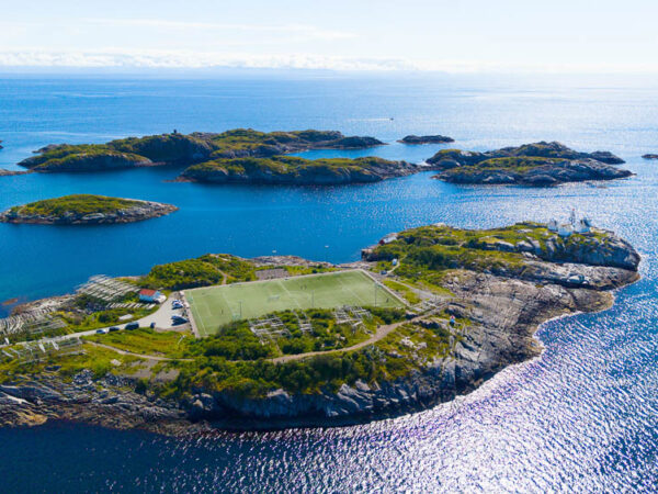 Bildet viser den verdenskjente fotballbanen i Henningsvær i Lofoten, som ligger spektakulært til på en liten, steinete øy omgitt av klart, blått hav.