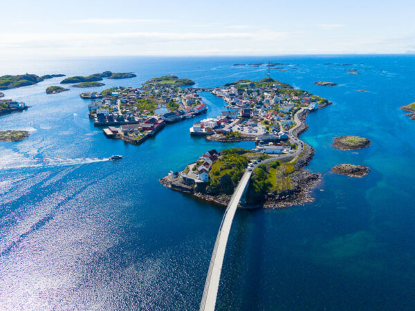 Et vakkert luftfoto som viser det idylliske fiskeværet Henningsvær i Lofoten omkranset av et klart, dypblått hav.