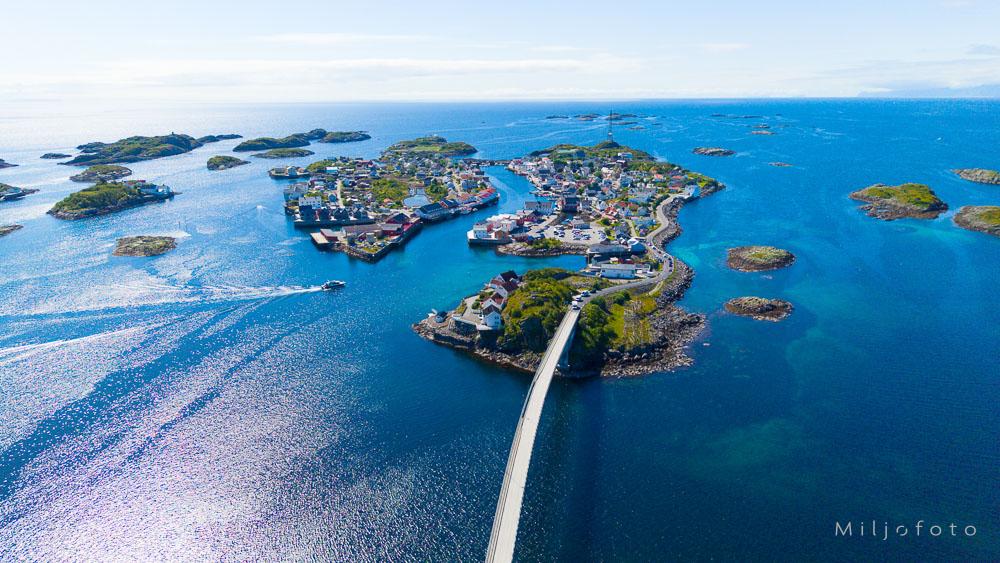 Et vakkert luftfoto som viser det idylliske fiskeværet Henningsvær i Lofoten omkranset av et klart, dypblått hav.