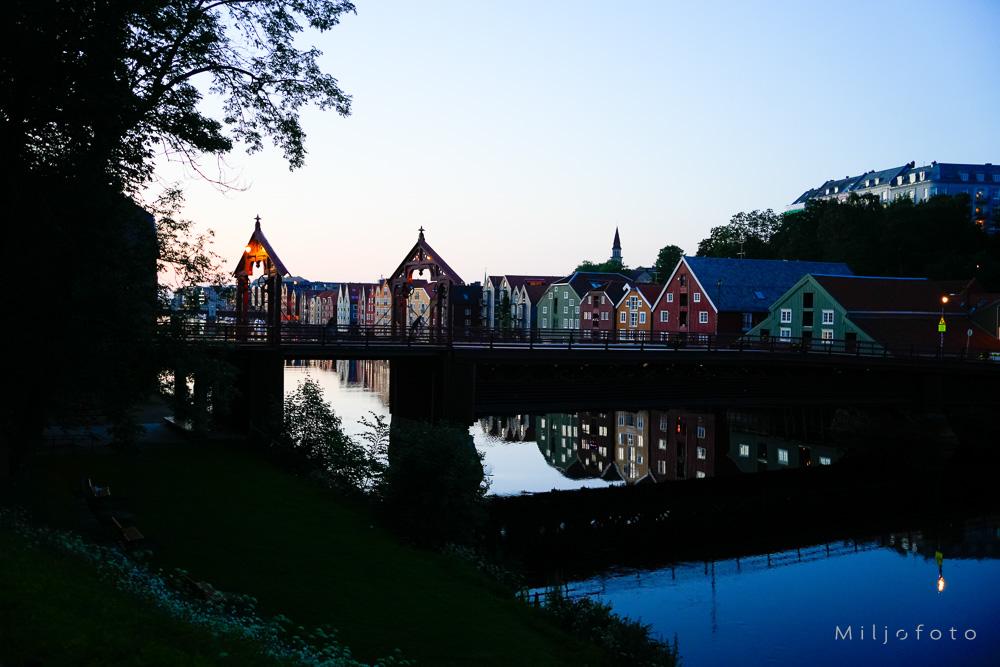 Bildet viser den ikoniske Gamle Bybro i Trondheim som strekker seg over Nidelva i det milde kveldslyset.