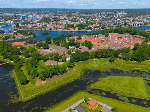 Bildet viser et vakkert luftfoto av Gamlebyen i Fredrikstad på en solrik sommerdag, preget av de karakteristiske stjerneformede vollgravene