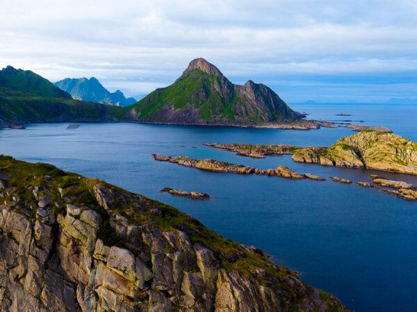 Bildet viser et vakkert og dramatisk kystlandskap fra Lofoten, med spisse, grønnkledde fjell som reiser seg opp fra det dype